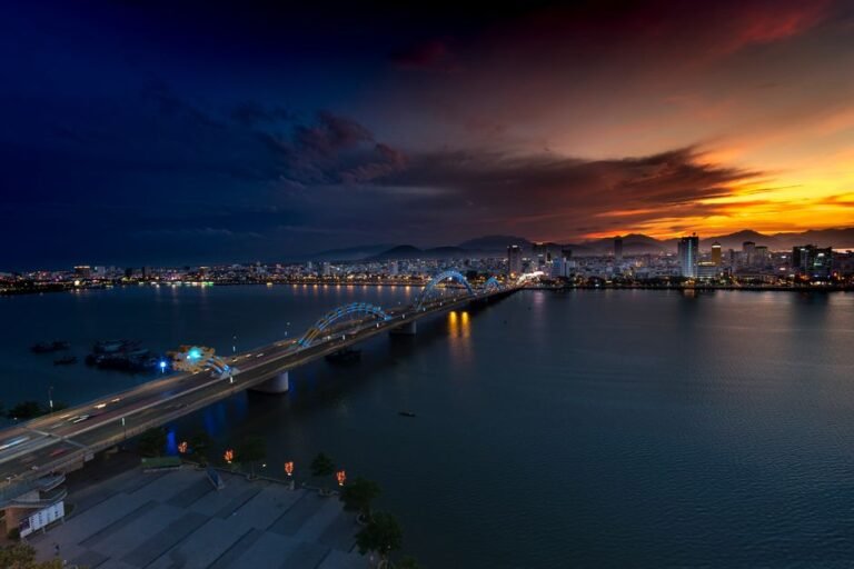 Toàn cảnh Đà Nẵng về đêm với Cầu Rồng phun lửa, các tòa nhà hiện đại và bãi biển Mỹ Khê lung linh.